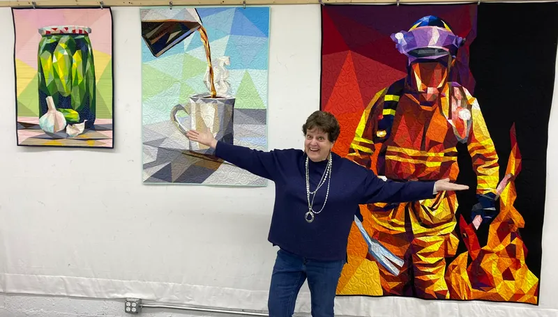 Mary Ellen with pickle jar, coffee, and firefighter quilts at show