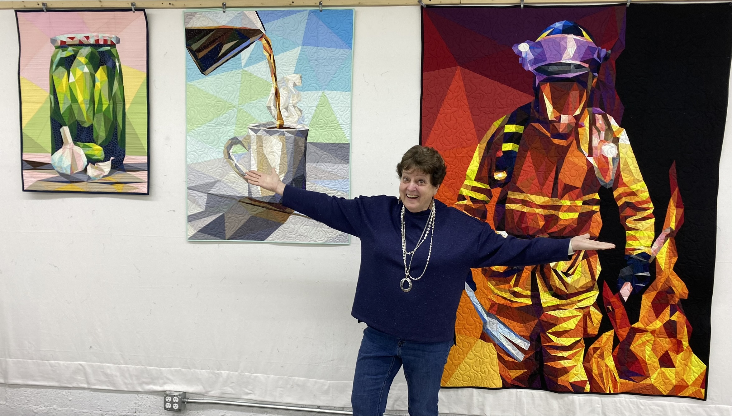 Mary Ellen with pickle jar, coffee, and firefighter quilts at show
